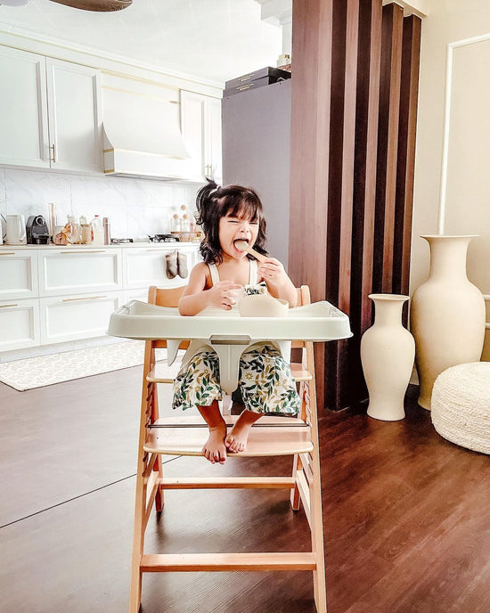 toddler girl on alpha high chair smiling with spoon in mouth