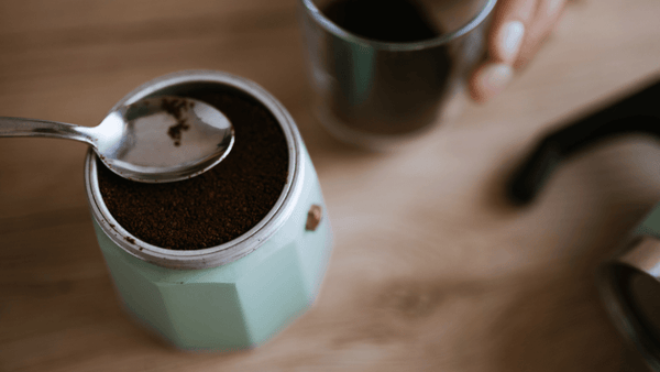 Mit einem Löffel streicht jemand das Kaffeepulver im Filtereinsatz eines Espressokochers glatt, ohne dieses anzudrücken.