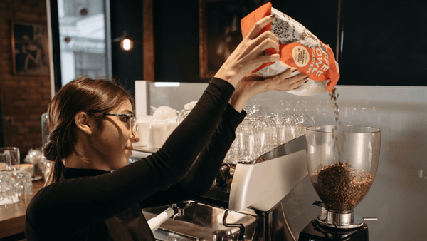 Eine Frau kippt Kaffeebohnen in den Behälter einer elektrischen Kaffeemühle.