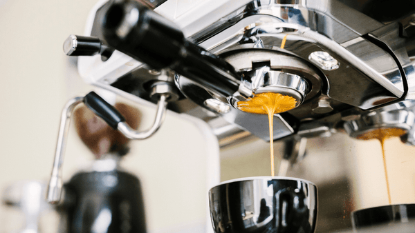Eine Siebträgermaschine kocht einen Espresso und man sieht den Kaffee durch das Sieb fließen.