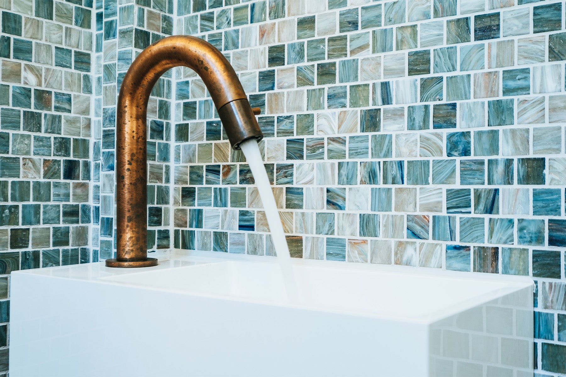 Hotbath basin faucet in Living Color Natural Brass against a vibrant blue tile background, showcasing the elegant design and timeless patina.