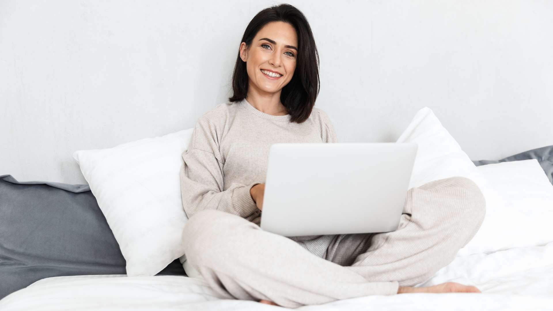 How much sleep do you need by age? Woman smiling using laptop in bed