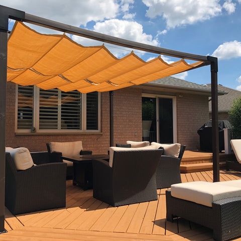 A backyard of a bungalow. The house has a wooden deck with a patio set and an orange backyard shade sail covering it.