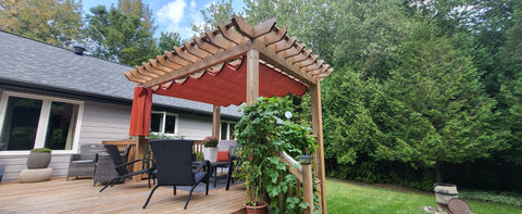 Small house backyard with a red pergola retractable shading the deck, adorned with patio chairs and lush greenery.