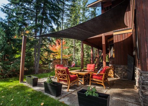 Image of a serene forest backyard with a cozy patio area adorned with a red backyard patio set, comfortably arranged beneath a protective backyard canopy, surrounded by lush greenery.