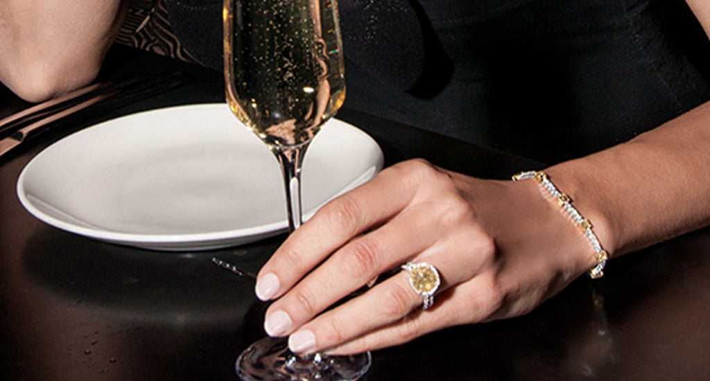 Woman holding champagne glass and wearing Shimansky fancy yellow jewellery