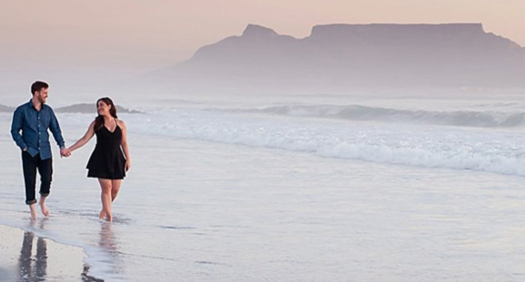 Happy couple walking on the beach with Table Mountain in the background