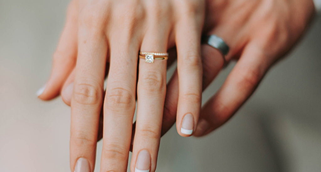 Woman wearing a Shimansky wedding ring hovering over a man's hand wearing a Shimansky wedding band