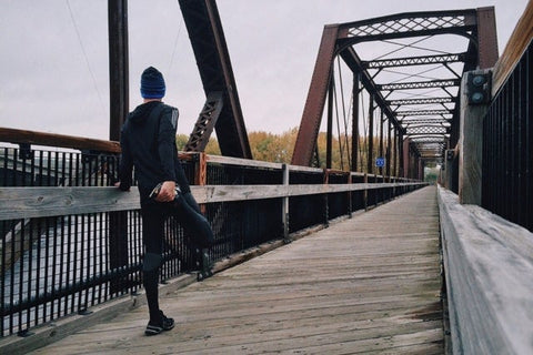 Runner wearing TXG compression socks stretching on a bridge