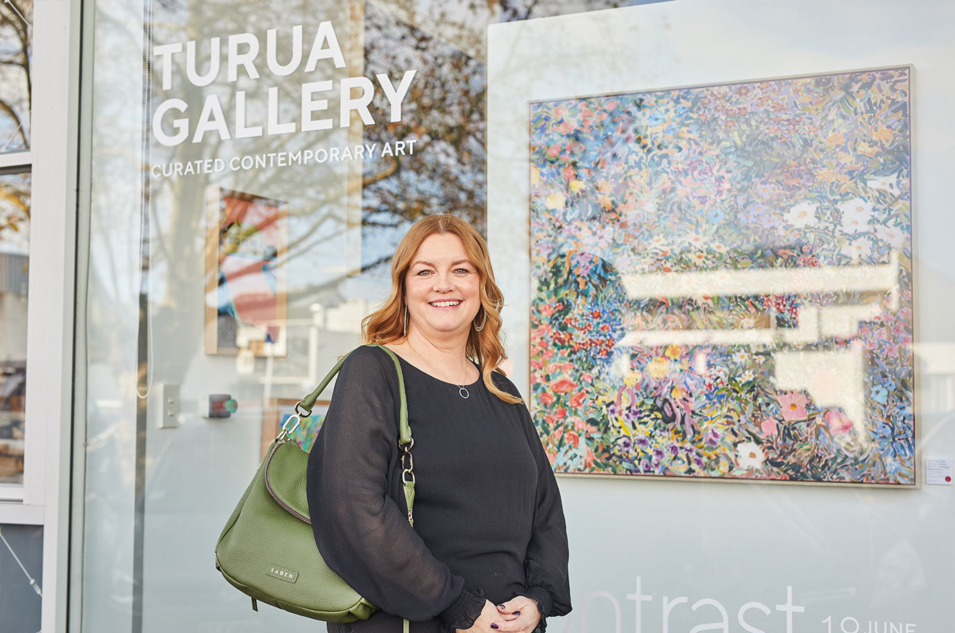 melissa from turua gallery standing in front of carmel van der hoeven painting with Saben handbag in ivy green