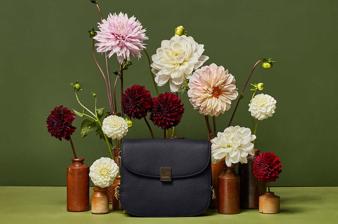 Saben black blaise handbag sitting amongst wild flower garden from the new collection
