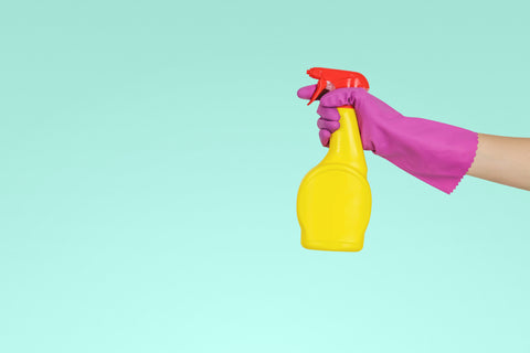 Main avec un gant rose de nettoyage et un vaporisateur jaune