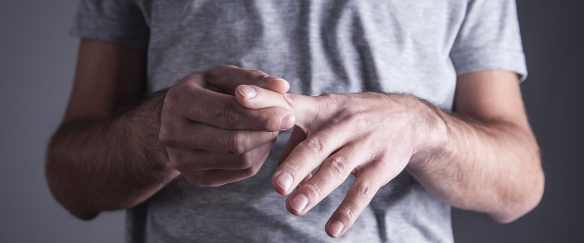 Mann hält sich den Finger aufgrund von Schmerzen durch Arthrose. Diese Schmerzen können mit einem TENS Gerät behandelt werden.