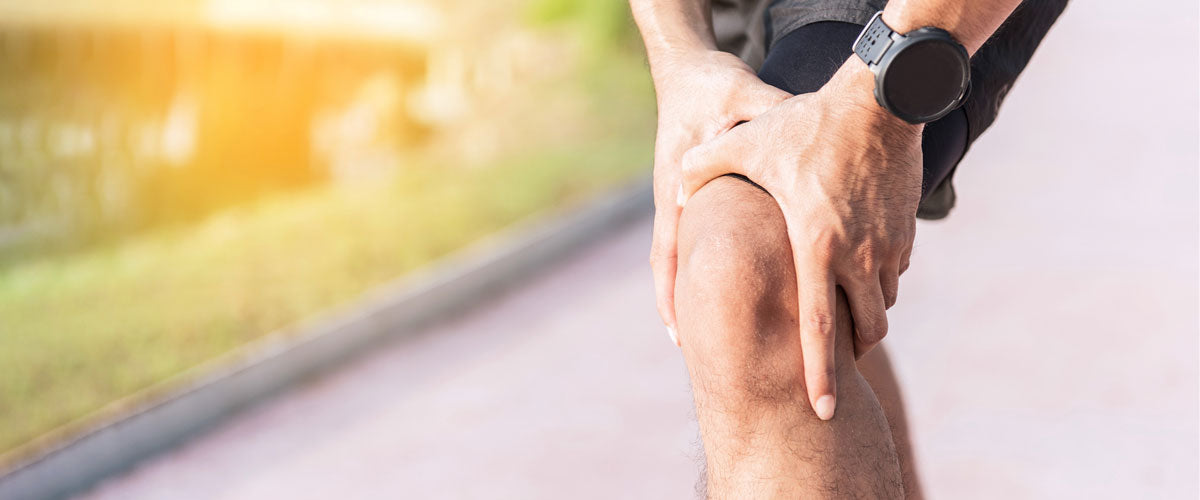 Män hält sich beim Laufen bzw. Joggen das Knie vor Schmerzen. Es könnte sich um einen Bänderriss handeln, welcher mit einem TENS Gerät behandelt werden kann.