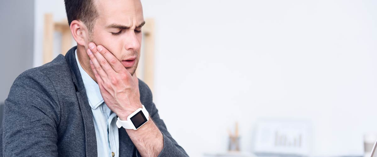 Man holding his face in jaw area due to pain from bruxism. Bruxism pain can be relieved with a TENS device.