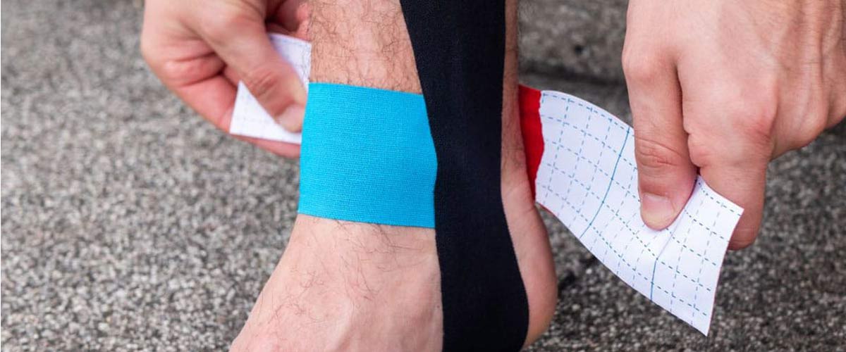 Mann bandagiert sich den Fuß um den Knöchelbereich mit Kinesiologie Tape