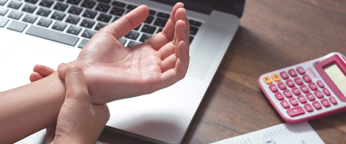 Homme tenant le poignet dans la douleur au bureau après avoir longtemps travaillé sur un ordinateur portable. Il pourrait s'agir d'un bras de souris.