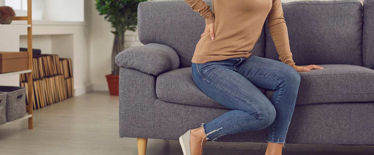 Woman sitting on a cocu and holding her lower back in pain. Pain in the lumbar spine can be treated with a TENS device.