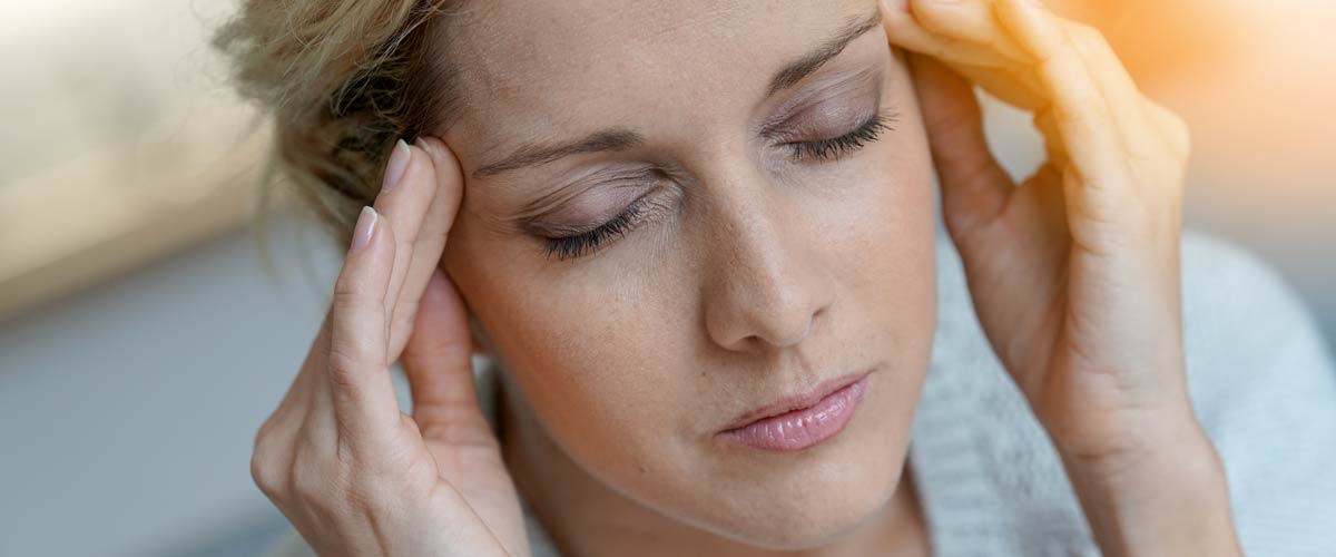 Frau hält sich die Schläfen und hat geschlossene Augen. Sie leidet an einer Migräne und hat Kopfschmerzen.