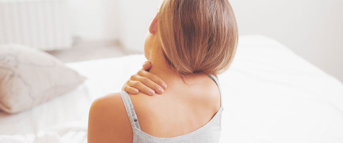 Frau zuhause im Schlafzimmer hält sich den Nacken aufgrund von Verspannungen und Schmerzen. Diese Schmerzen können mit einem TENS Gerät behandelt werden