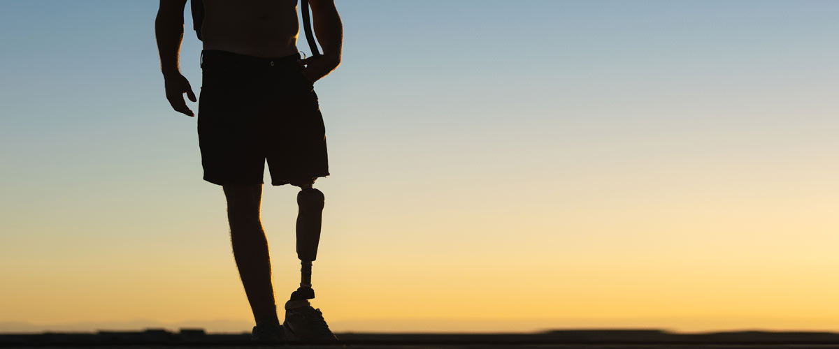 Homme avec jambe prothétique au coucher du soleil. Les personnes amputées de parties du corps ressentent souvent une douleur fantôme, qui peut être traitée avec un appareil TENS.