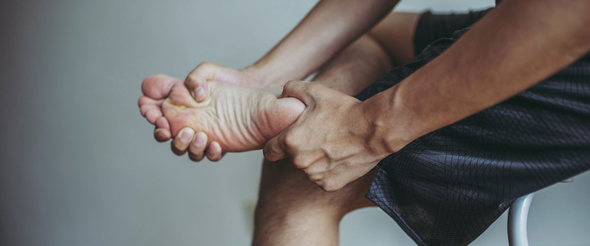 Mann hält sich den Fuß aufgrund von Schmerzen, die durch Polyneuropathie ausgelöst werden. Patienten beschreiben das Gefühl wie Ameisen unter der haut. Ein TENS Gerät kann helfen.