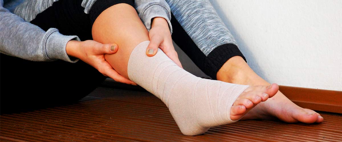 Frau hält sich das Sprunggelenk aufgrund von Schmerzen, es ist auch bandagiert. Diese Schmerzen können Sie mit einem TENS Gerät behandeln.