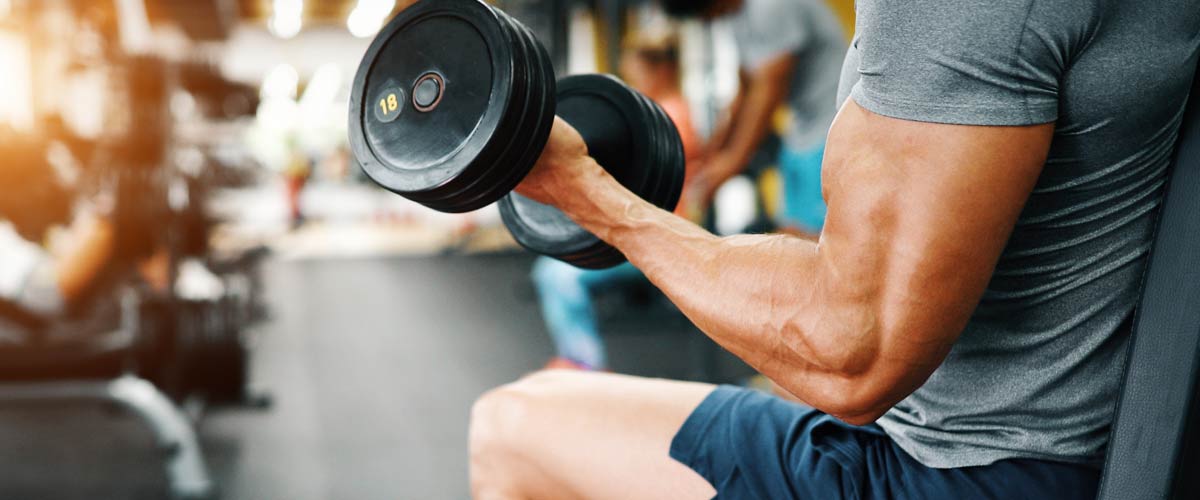 Homme dans la salle de gym faisant des boucles de biceps avec une machine EMS et des haltères