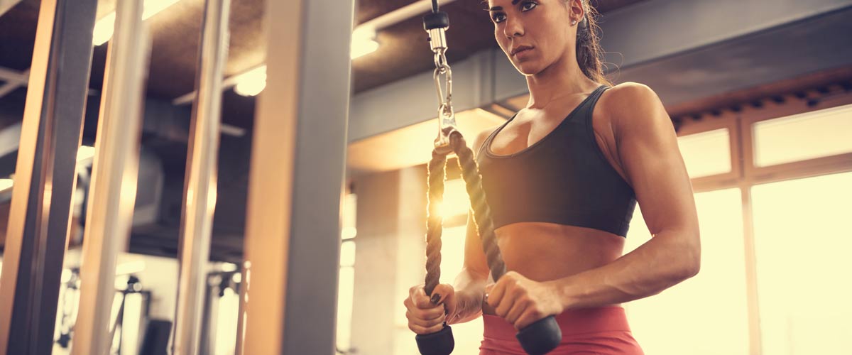 Woman trains her triceps on a cable pull, in addition to the EMS device