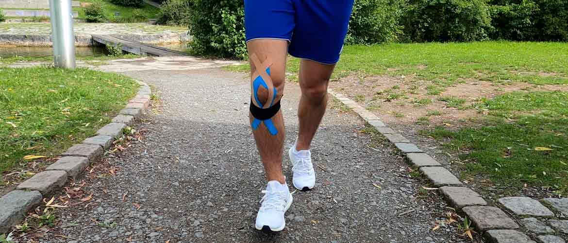 L'homme fait du jogging et a son genou bandé avec du ruban de kinésiologie pour la stabilisation