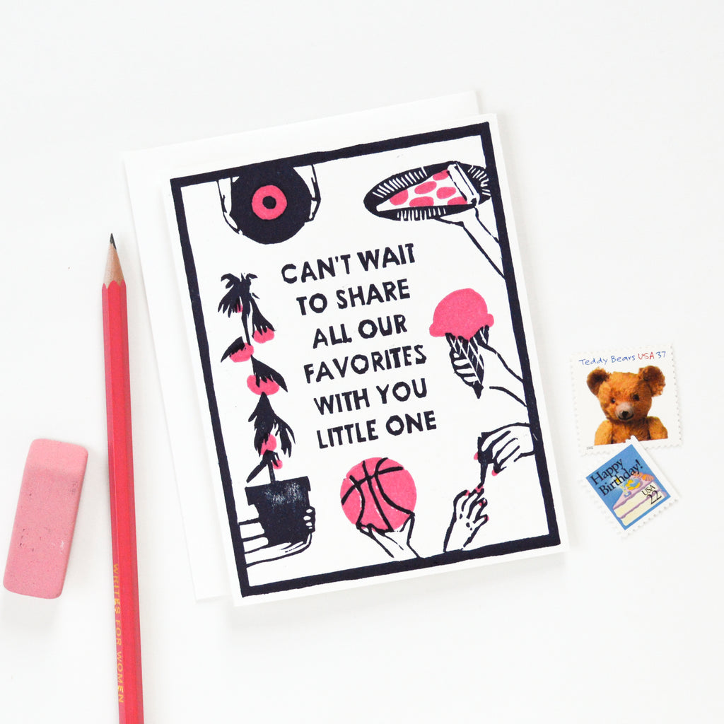 Handmade new baby card that says "Can't Wait to Share All Our Favorites With You Little One" with a woodcut image of hands holding out a record, a slice of pizza, an ice cream cone, a basketball, and a tomato plant in navy blue and pink. 