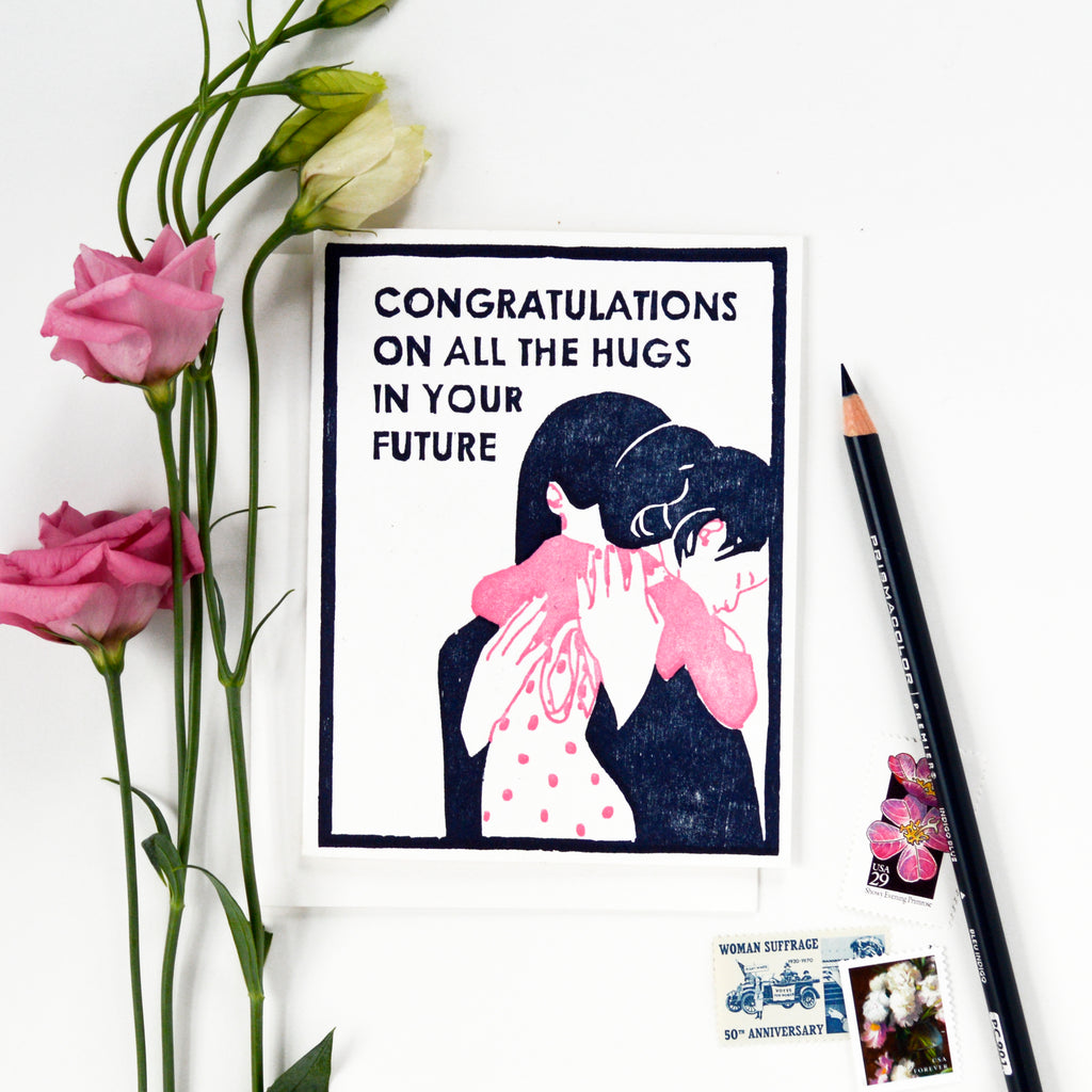 Handmade new baby card that says "Congratulations on all the hugs in your future" on it with a woodcut image of a mother hugging a little girl.