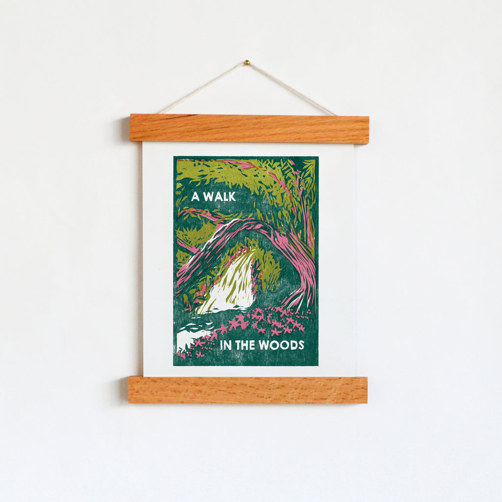 Digital art print designed using hand-carved woodblocks of a tree and a path in the woods in green and pink that says "A Walk in the Woods."