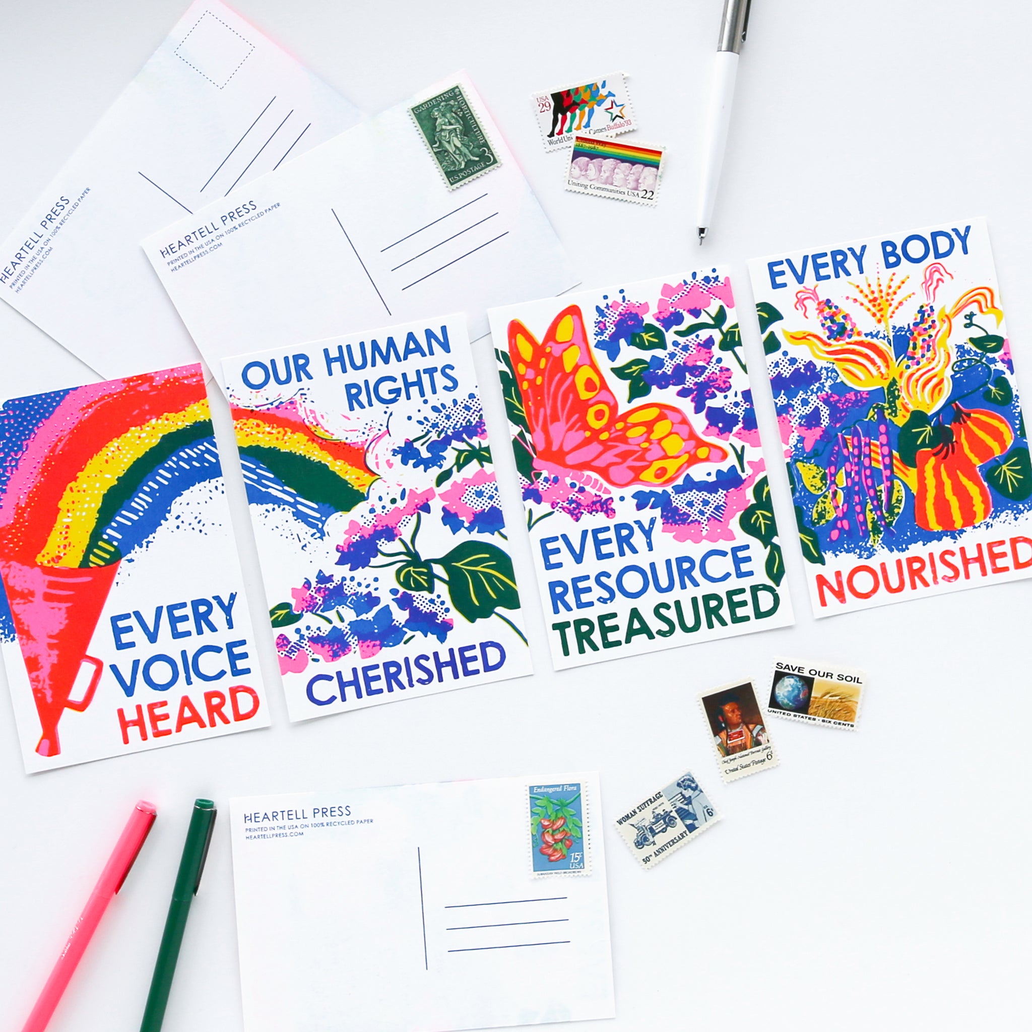 Four social change activism risograph postcards in bright pink, yellow and blue with pens and stamps