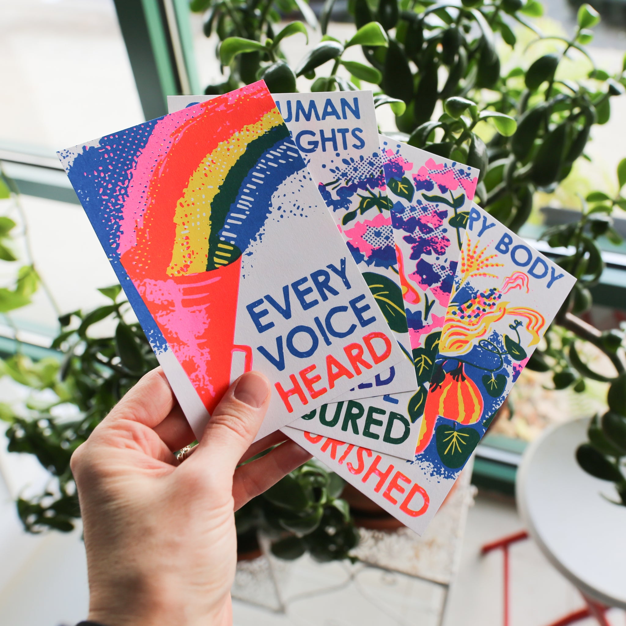 a hand holding a postcard with a rainbow coming out of a bullhorn that says "every voice heard"