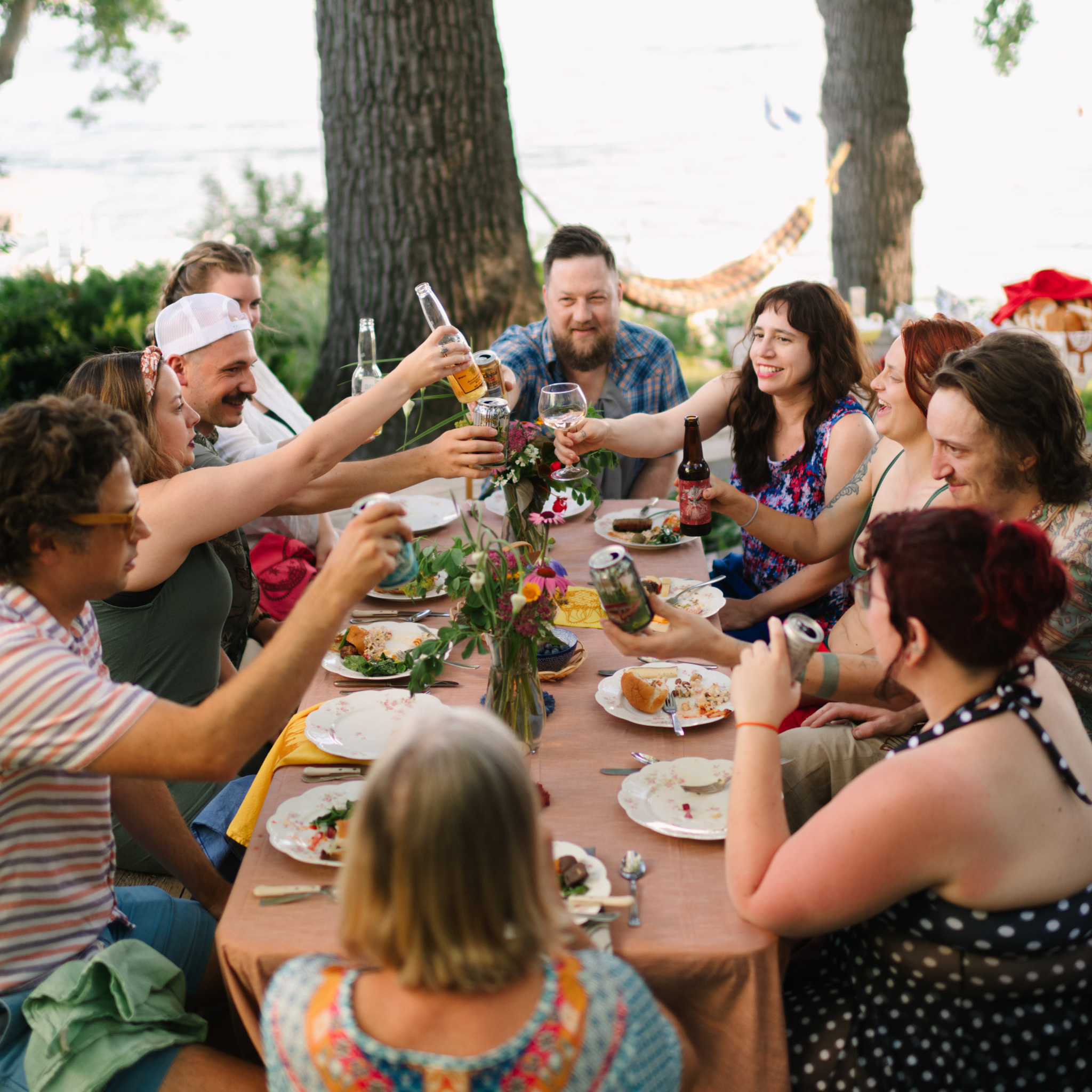 a group of people sitting outside around a table making a toast and saying cheers