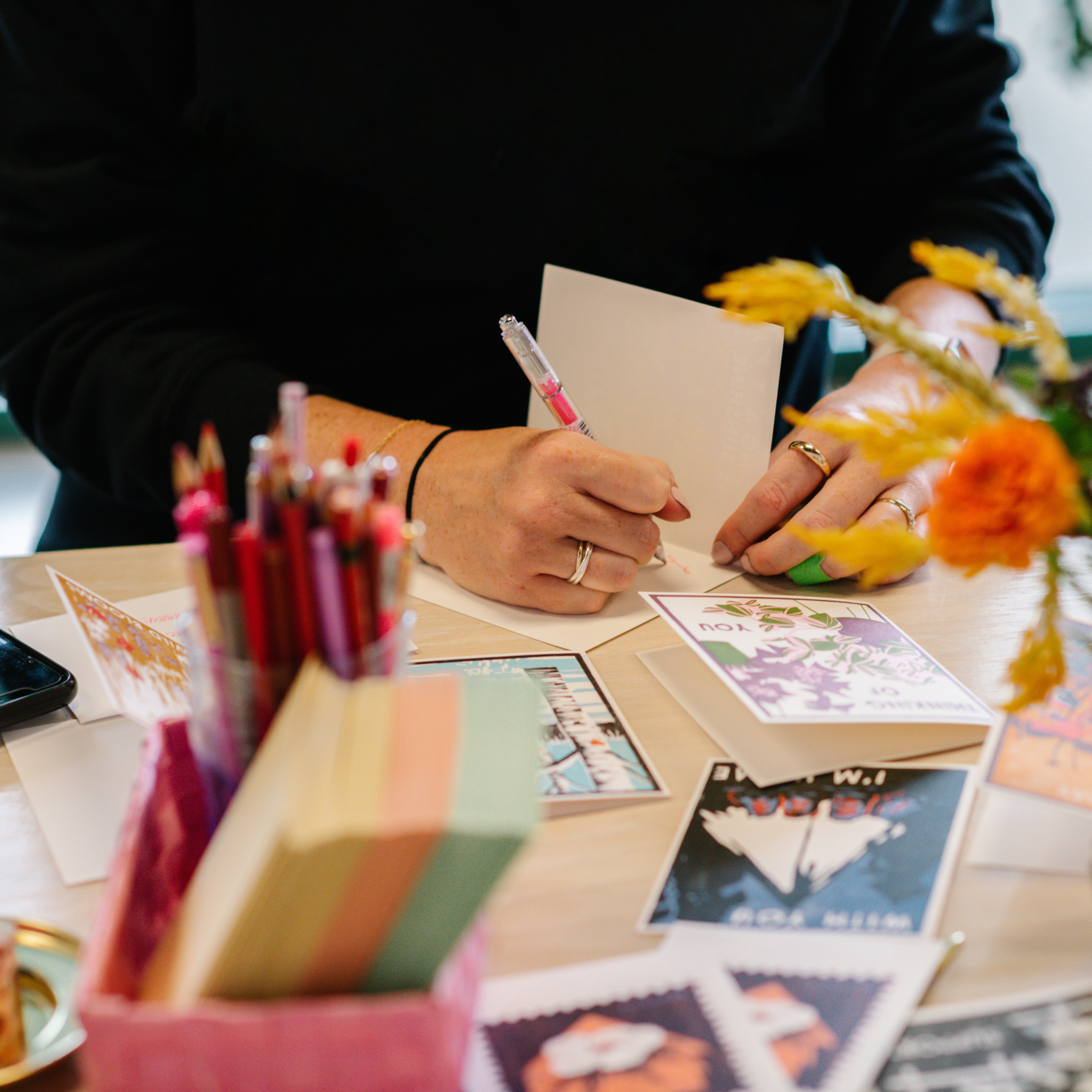 a person writing a note in a greeting card with other cards and pens in the foreground