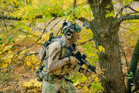 Airsoft Canada player in full tactical gear holding an airsoft rifle while stealthily navigating a wooded area with yellow autumn leaves.