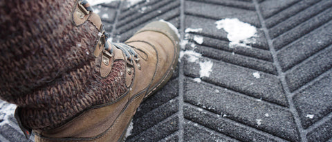 Closeup of WaterHog Luxe In Vein Rugged Doormat wiping snow from the bottom of a boot.