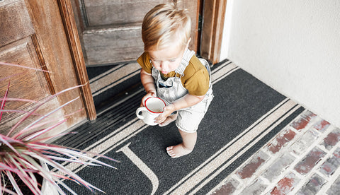 Child walking across double door personalized monogram doormat at front door.