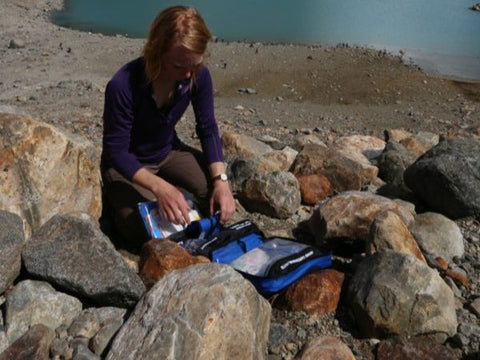 Woman looking at first aid kit on rocks in front of water