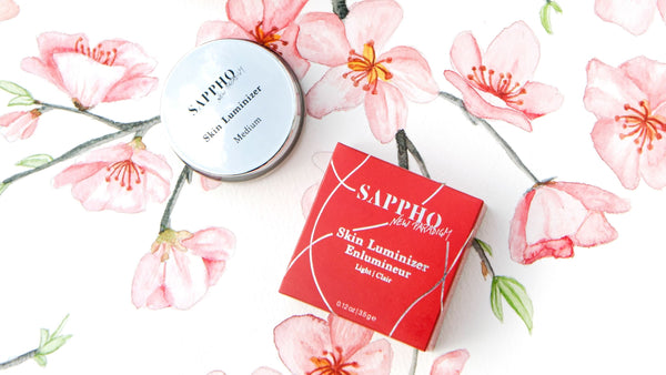 Vegan SKin Luminizer pot and red box packaging scattered over cherry blossom painting