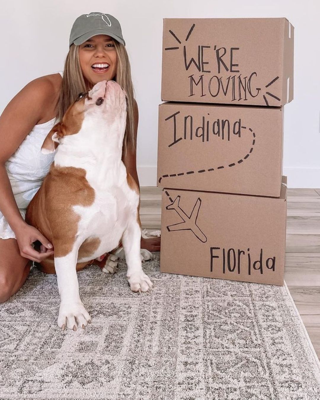Larissa white sits on the Carina rug next to her pup and stacked boxes with "We're moving from Indiana to Florida" written on them.