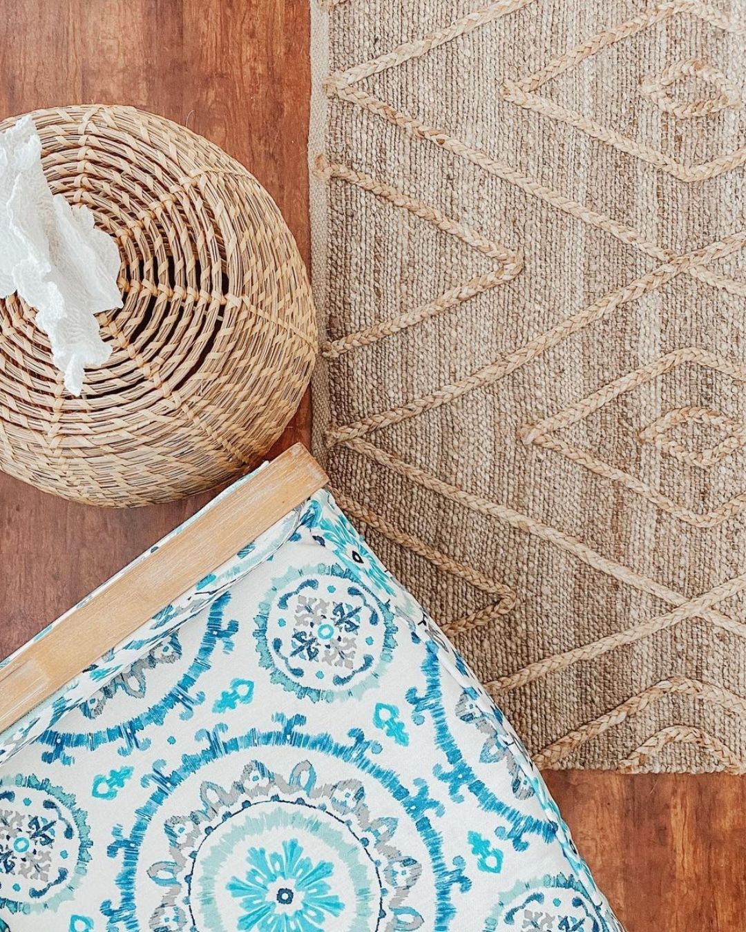 Top down photo of a patterned chair, textured jute rug and a wicker side table with a piece of white coral on top.