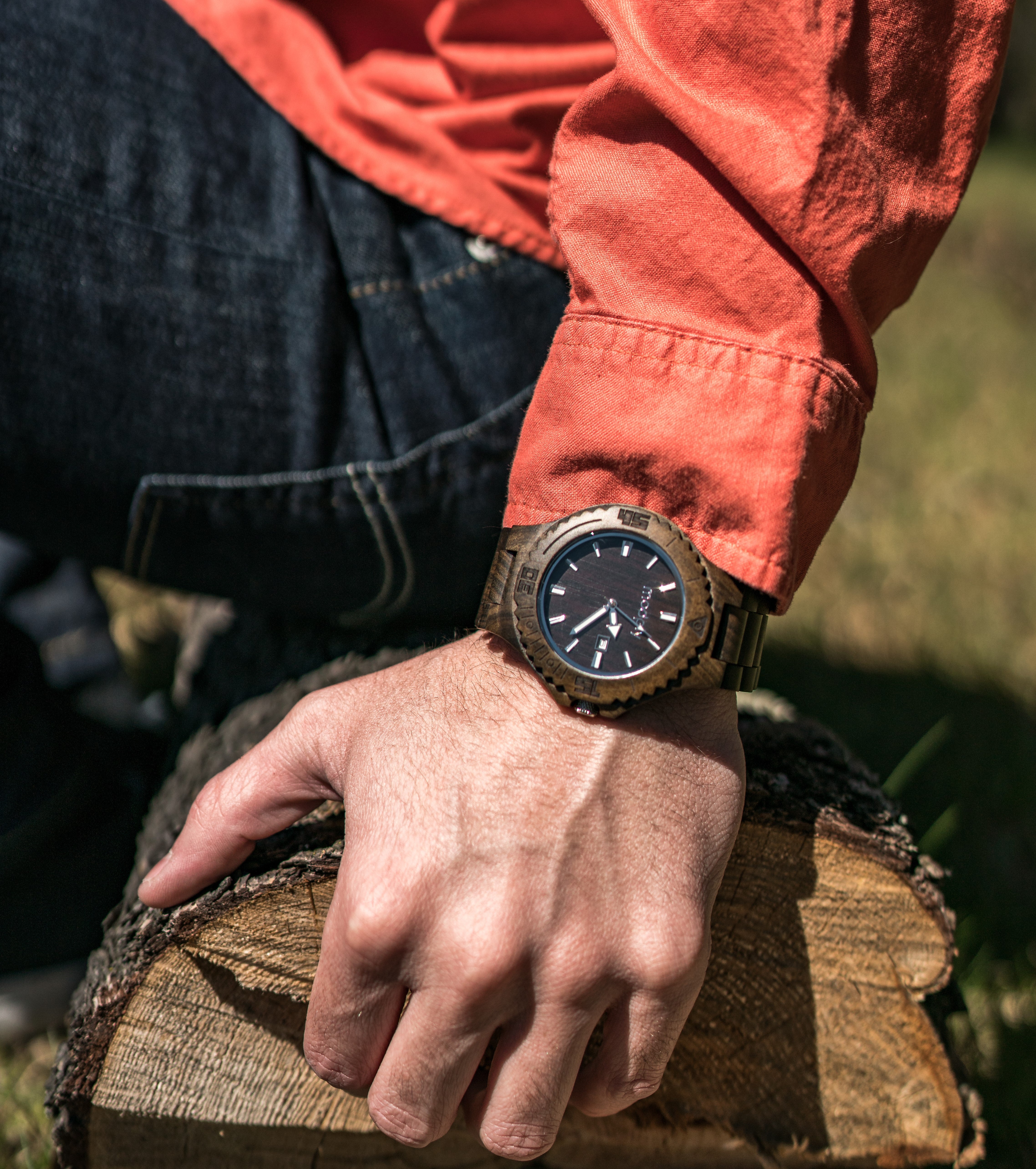 Hand wearing a wooden watch, gripping a log.