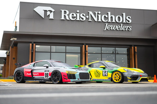 Two race cars in front of Reis-Nichols Jewelers storefront.