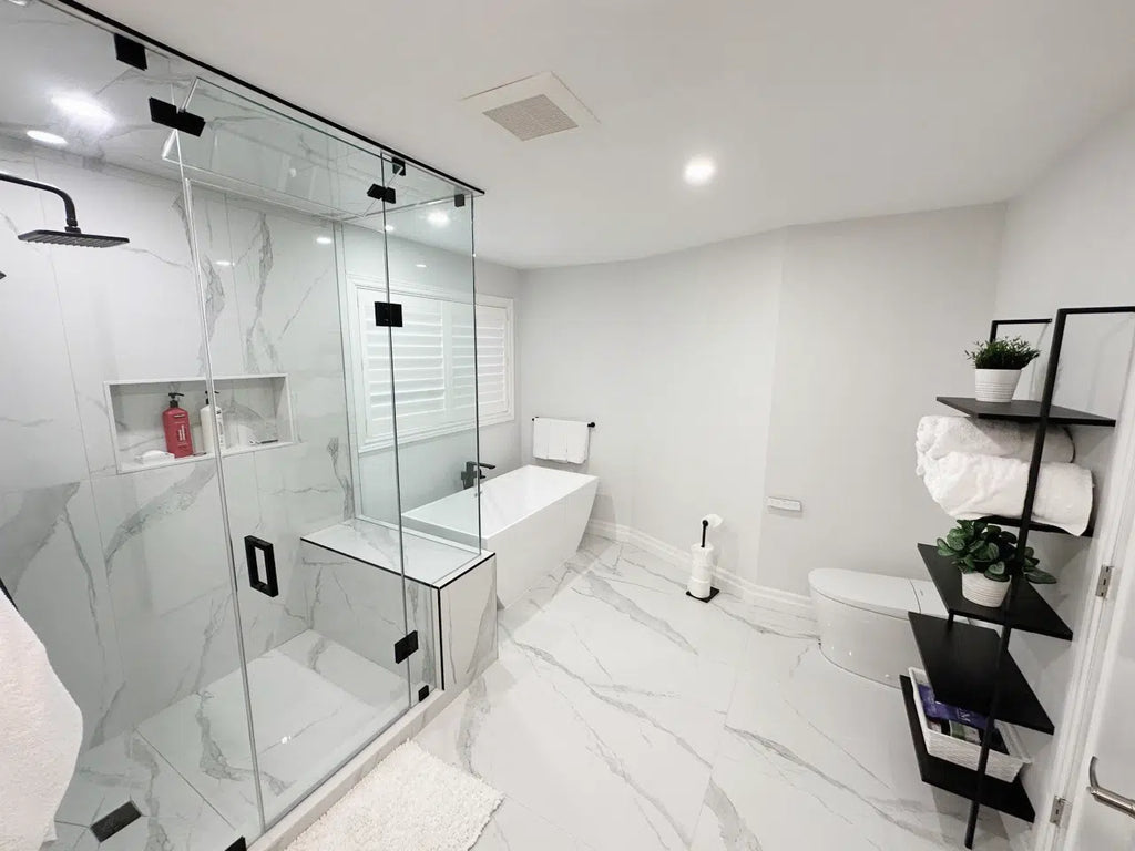 A sleek and contemporary bathroom with a glass-enclosed shower, white bathtub, towel rack with a large white towel, small potted plant, white shutters, and a stack of white towels.