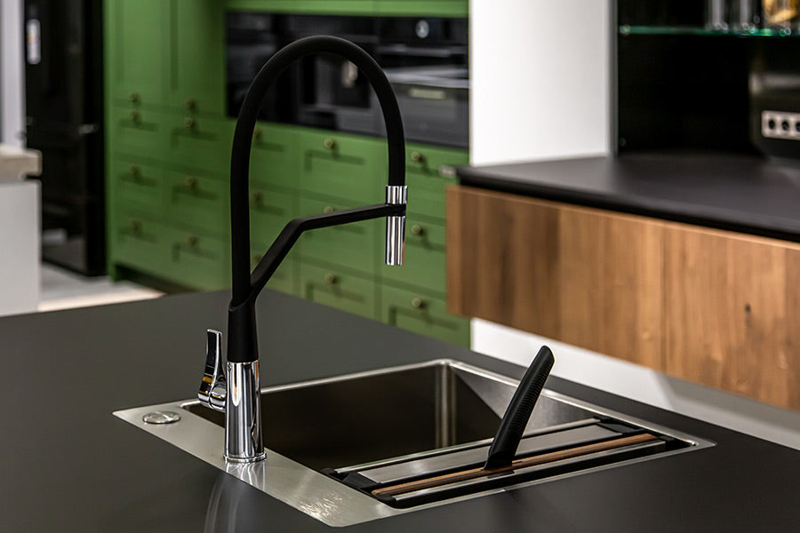 This modern kitchen features vibrant green cabinets and a contrasting black sink. A pen in the sink hints at a creative environment, while a black refrigerator compliments the colour scheme.