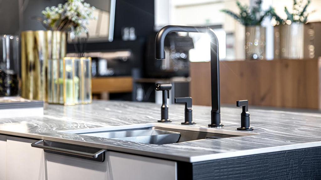 Contemporary kitchen with black marble countertop, stainless steel sink, gold vase.