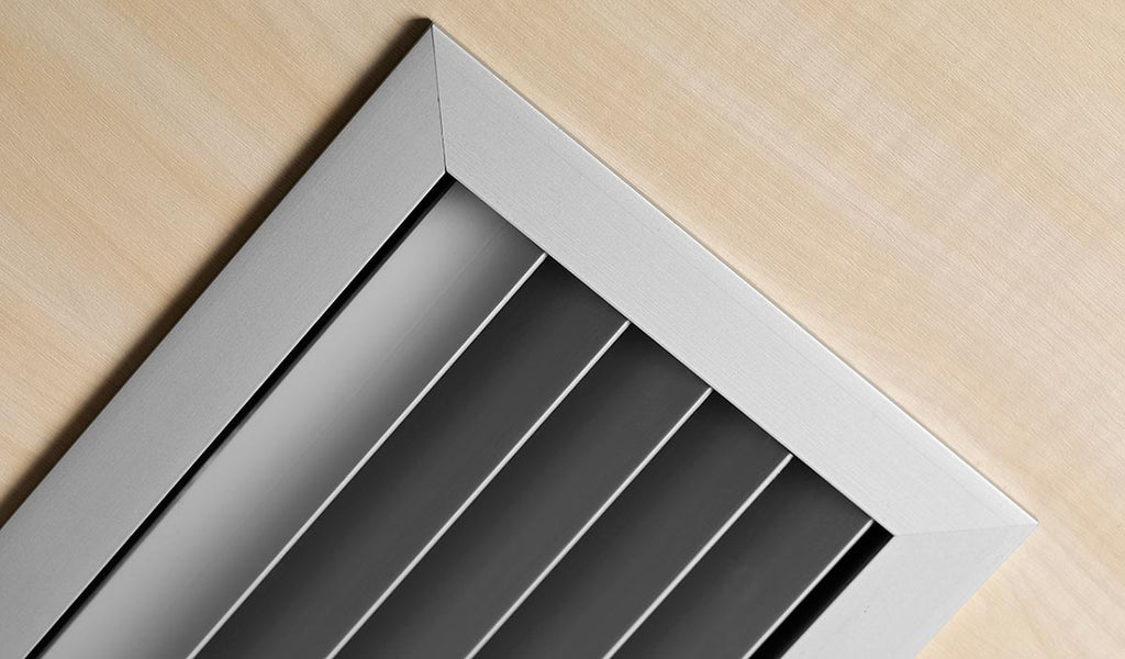 A detailed metal grille on a wooden surface, adjacent to a sleek black and white radiator, showcasing intricate design and contrasting textures.